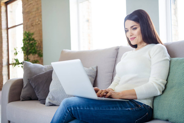 Portrait of her she nice attractive lovely cute cheerful focused girl typing e-mail using laptop sitting on divan in light white interior living-room indoors - Fotografie, Obrázek