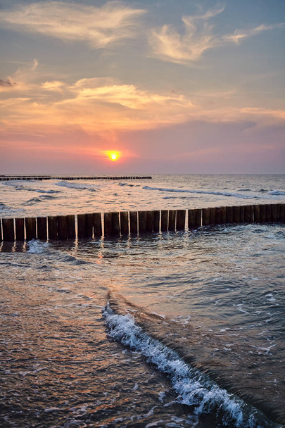 Ξύλινος θραύστης που παρατηρείται από μια παραλία στο ηλιοβασίλεμα. - Φωτογραφία, εικόνα