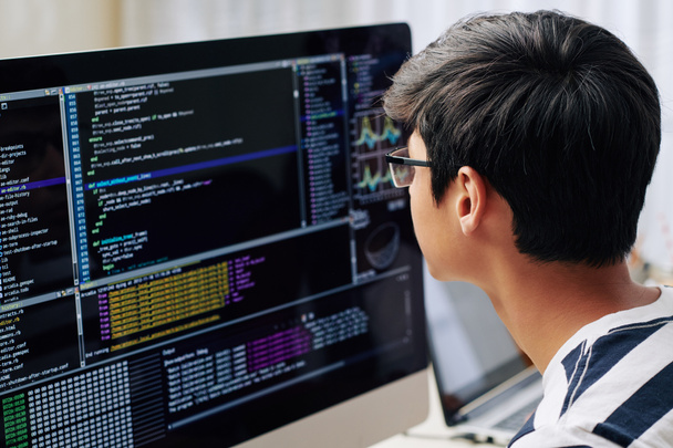 Adolescente inteligente en gafas comprobando el código de programación en la pantalla de la computadora cuando está sentado en su escritorio
 - Foto, imagen
