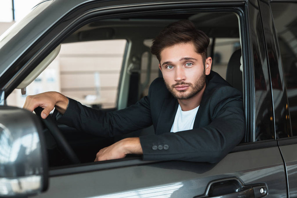 handsome man sitting in brand new car after succesful deal in dealership center feeling happy - Foto, Imagem