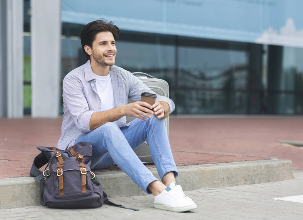 Young male traveller sitting near airport terminal with coffee - Photo, Image