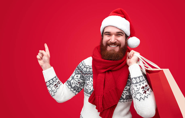 Cheerful guy with Christmas purchases pointing aside - Photo, image