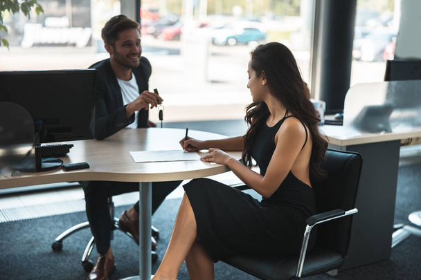 handsome man manager holding deal with beautiful woman client at dealership office - Photo, image