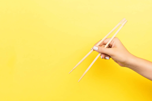 Рука дівчинки показує палички на жовтому тлі. Поняття азійської кухні з порожнім простором для вашого дизайну. - Фото, зображення