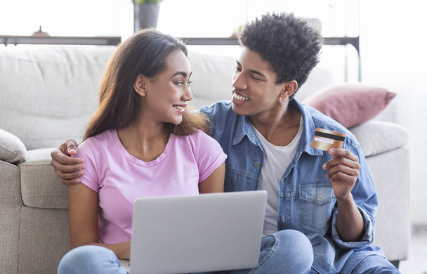 Nuori afrikkalainen pari ostoksia verkossa, kannettavan tietokoneen ja luottokortin avulla
 - Valokuva, kuva