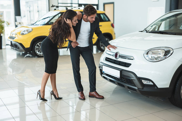 beautiful young couple man and woman looking for a brand new car in dealership center - Foto, immagini