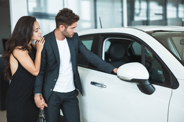 beautiful young couple man and woman choosing a brand new car in dealership center - Foto, Imagen