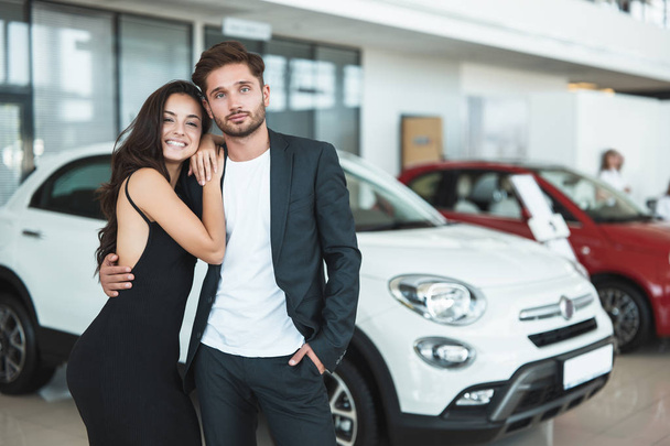 beautiful young happy couple man and woman choosing a brand new car standing in dealership center - Zdjęcie, obraz