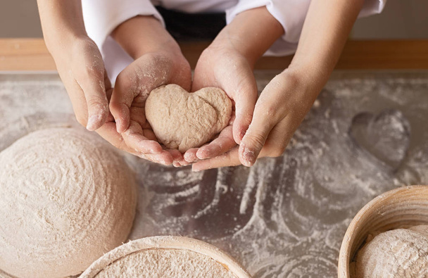 Crop bakers showing heart from dough - Foto, afbeelding