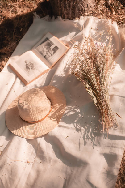 Σύνθεση από ένα βιβλίο, λουλούδια και ένα γυναικείο καπέλο στο πάρκο στο γρασίδι. - Φωτογραφία, εικόνα