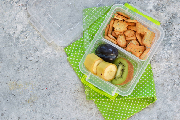 Lunch box with fruit: banana, kiwi, plum. Top view. - Foto, afbeelding
