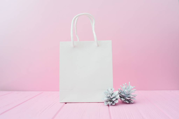 Karácsonyi ajándékot csomagolás háttérben. Flat feküdt fehér kézműves csomag és kúp rózsaszín fából készült háttér. Modern életmód összetétele skandináv stílusban - Fotó, kép
