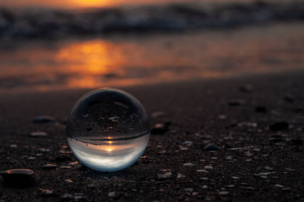 glass ball  on sandy beach against blurred sea background  - Foto, Imagen