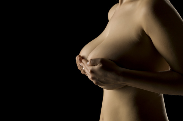 Woman holds her big breasts with her hands on black background - Фото, зображення