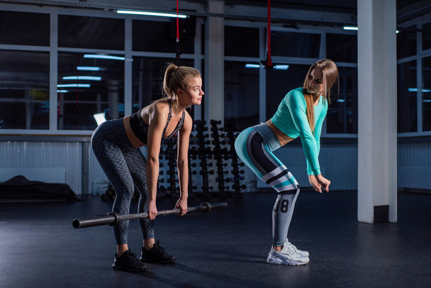 Young sports girl does deadlift with a barbell in the gym under the supervision of a trainer. Female trainer teaches ward deadlift. Personal training. Exercises on the buttocks. - Foto, Imagem