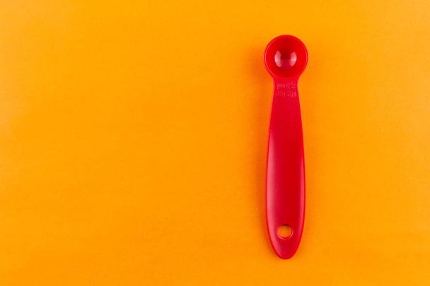 measuring spoon of plastic on orange background. - Фото, изображение