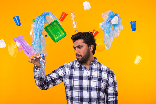 Problema de reciclaje de plástico, ecología y concepto de desastre ambiental: sorprendido hombre indio sosteniendo una botella de plástico arrugada sobre un fondo amarillo
. - Foto, Imagen
