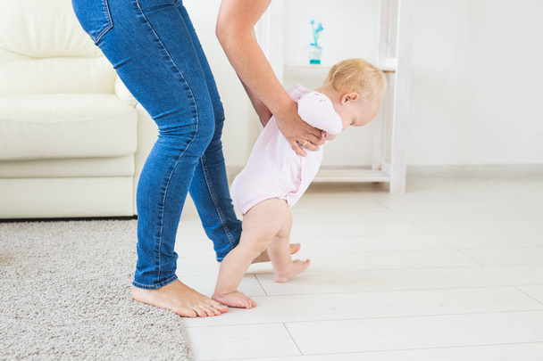 Die ersten Schritte des Kleinkindes, das im weißen, sonnigen Wohnzimmer laufen lernt. Schuhe für Kinder. - Foto, Bild