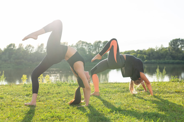 Healthy lifestyle and people concept - Flexible women doing yoga in the summer park - Foto, Imagen