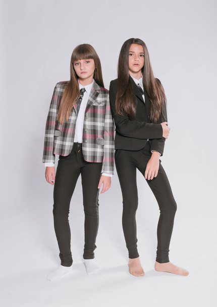 Two cute girls schoolgirls in a trendy school uniform on a white background. School fashion. Children's school fashion clothes - Foto, Imagen