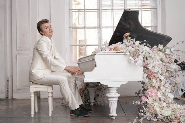 屋内だけで白い大きなグランドピアノを持つ若いティーンエイジャーの男は、音楽を楽しんでいます - 写真・画像