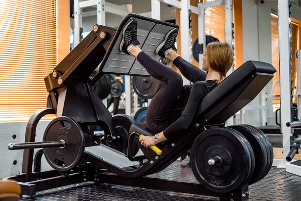 De jonge sportieve vrouw doet been oefeningen op de machine van de been pers - Foto, afbeelding