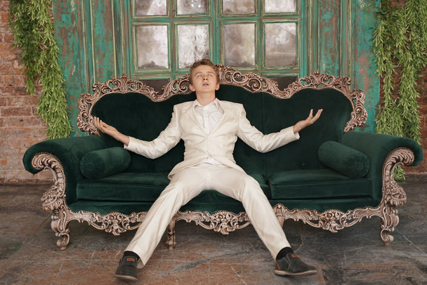 tired sleepy fashionable young man teenager stretches and yawns slightly in a white classic business suit on the background of a luxurious room - Foto, Bild
