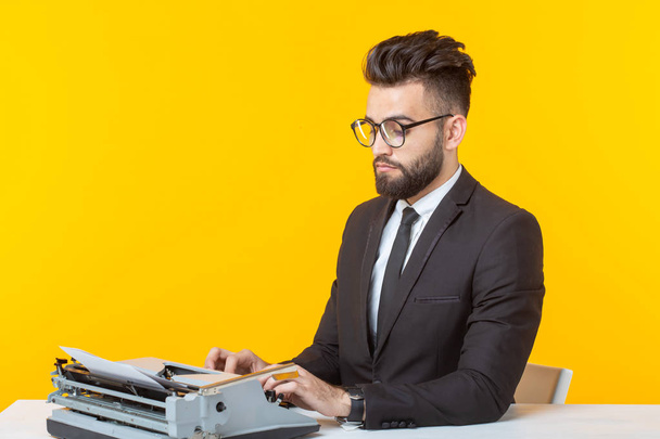 Arabischer Geschäftsmann oder Manager im formellen Anzug tippt Text auf einer Schreibmaschine auf gelbem Hintergrund. Konzept der Geschäfts- und Büroarbeit - Foto, Bild