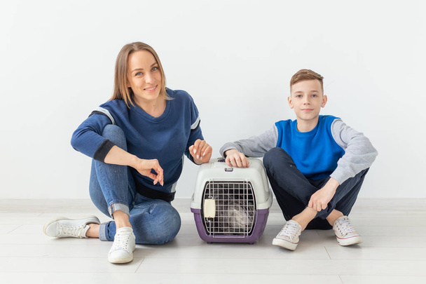 Positive good-looking mother and son launch their beautiful gray Scottish Fold cat into their new apartment after the move. Housewarming concept. - Foto, afbeelding