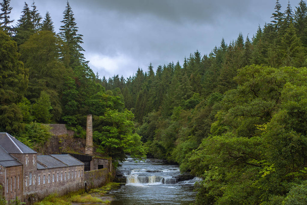 Водопады и здания старой мельницы, окруженные лесом на реке С
 - Фото, изображение