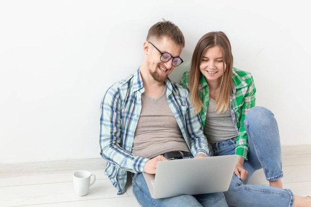 Lachend jong stel maakt online aankopen van meubels in hun nieuwe hypotheek appartement. Online Shopping concept met laptop en gadgets. - Foto, afbeelding