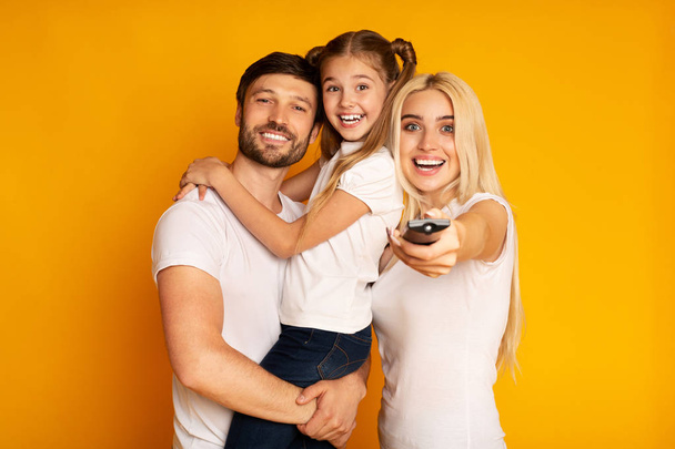 Boldog szülők és lánya kapcsolási csatornák tévénézés, stúdió shot - Fotó, kép