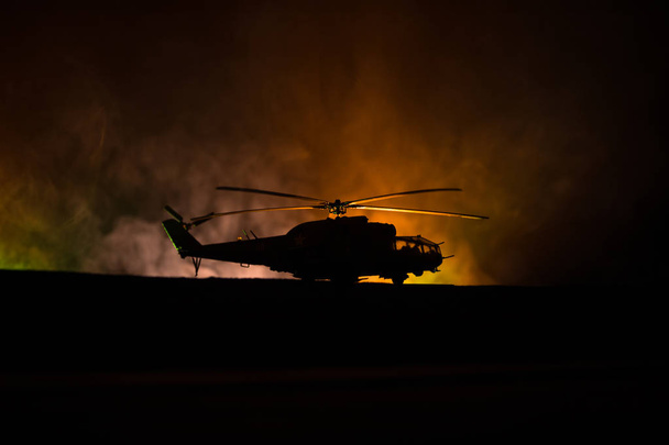 Σιλουέτα του Στρατιωτικό ελικόπτερο έτοιμο να πετάξει από την ζώνη σύγκρουσης. Διακοσμημένα νύχτα πλάνα με ελικόπτερο ξεκινώντας στην έρημο με ομίχλη τονισμένο με οπίσθιο φωτισμό. Επιλεκτική εστίαση. - Φωτογραφία, εικόνα