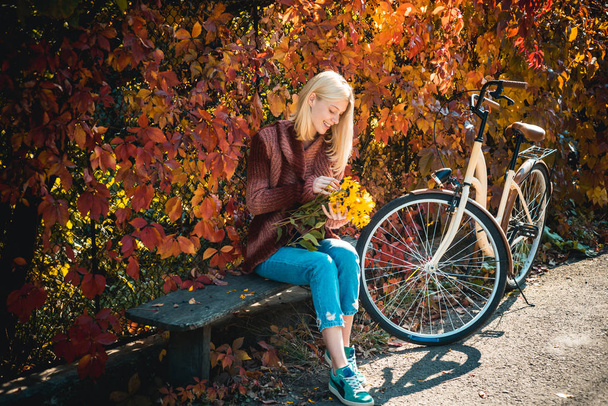 Dreamy girl with blonde hair in knit sweater. Beautiful young brunette sitting on a fallen autumn leaves in a park. Autumn Clothing and color trends. - Foto, Bild