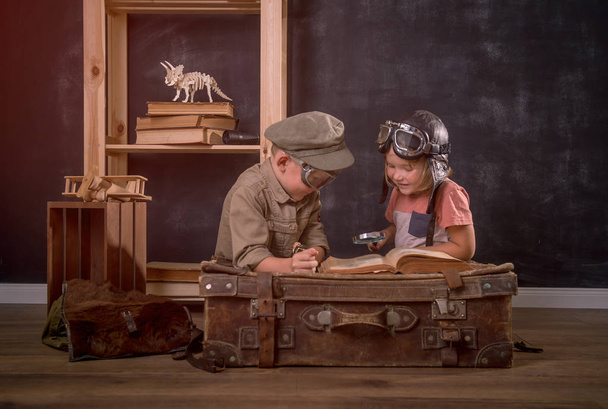 Een jongen en een meisje die piloot spelen. Vintage retro kinderportret in bril zittend op oude koffer met verrekijker en kompas in handen. Innovatie, reizen en onderzoek. - Foto, afbeelding
