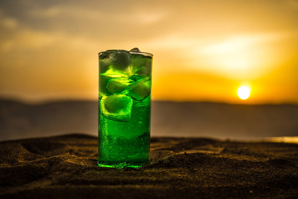 Закройте мокрый стакан зеленого холодного мятного напитка, цветной оранжевый фон заката на террасе. Охладительный летний напиток. Летнее свежее и охлаждающее вдохновение, сочетание вечернего контраста
. - Фото, изображение