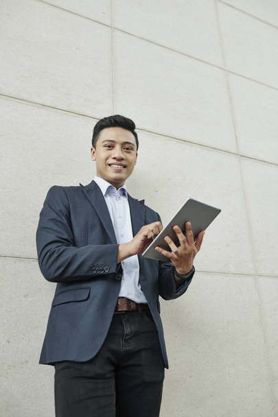 Весёлый молодой азиатский предприниматель, работающий над цифровыми планшетами и рассылающий электронные письма
 - Фото, изображение