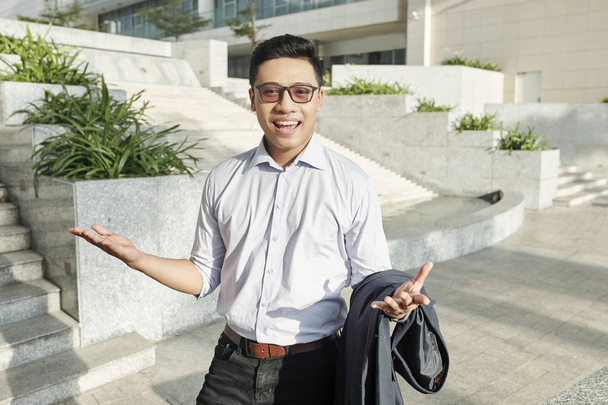 Позитивный возбужденный молодой вьетнамский бизнесмен в очках стоит на улице
 - Фото, изображение