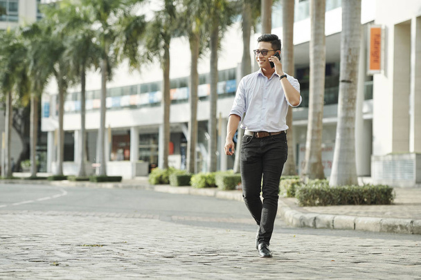 Bello fiducioso giovane asiatico uomo a piedi in città strada e fare telefonata
 - Foto, immagini