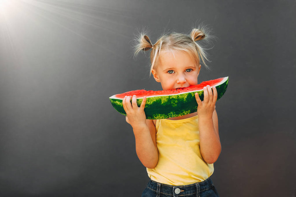 Funny kid eating watermelon outdoors on the gray backgrounds.   - Foto, immagini