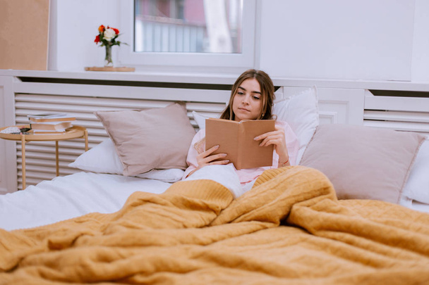 Kobieta czytając książkę leżąc w łóżku, nowoczesny design wokół - Zdjęcie, obraz