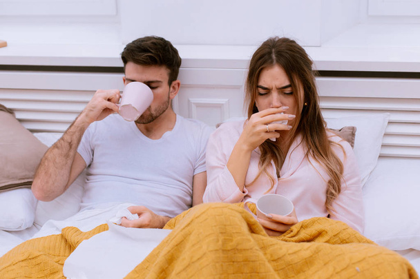 Hoesten paar in de ochtend hebben een griep en loopneus man drinken iets warm van een kopje en loopneus ze met behulp van weefsel voor neus - Foto, afbeelding