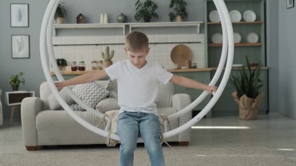 Little boy having fun on swing in living room. Happy son playing indoors in slow motion - Filmagem, Vídeo