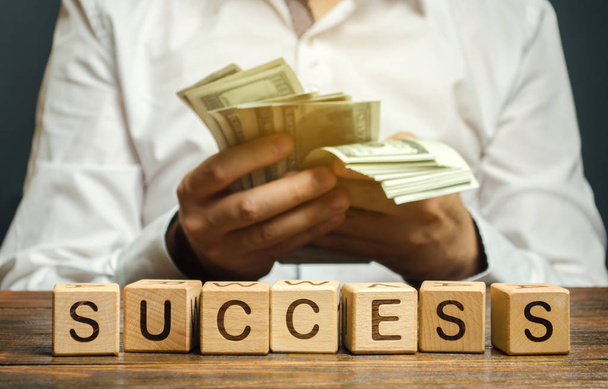 Wooden blocks with the word Success and businessman with money. Successful business concept. The growth of profits and earnings. Performance. Achieving the goal. Return on investment and profitability - Fotoğraf, Görsel