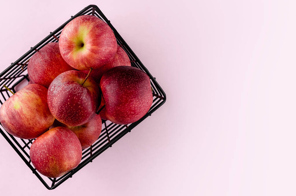 Red apples in the metallic black basket on the light pink background. Top view flat lay composition. Space for text template. Fresh autumn fruit wallpaper. - Zdjęcie, obraz