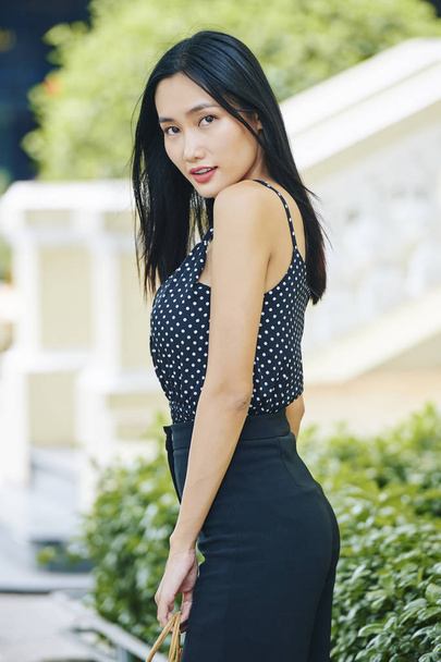 Retrato de una joven asiática con el pelo largo y negro usando ropa elegante y mirando a la cámara de pie al aire libre
 - Foto, imagen