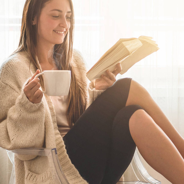 Piękna dziewczyna czyta książkę z filiżanką gorącej herbaty. Jesień zima czas. - Zdjęcie, obraz