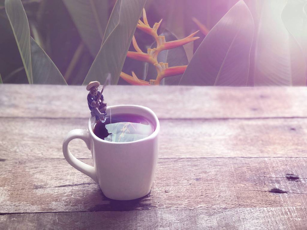 Café negro en taza blanca, Miniatura de pescador sentado y pescando, relajado en el borde de la taza, en café americano, espacio libre para su texto, con destello de lente, enfoque selectivo
. - Foto, imagen