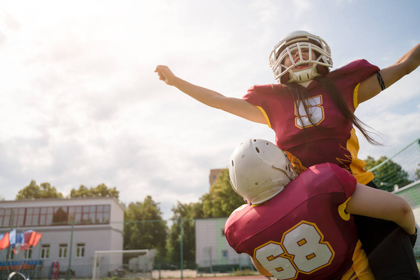 Image of two American football sportswoman wearing helmets with their hands to side against cloudy sky - Foto, afbeelding