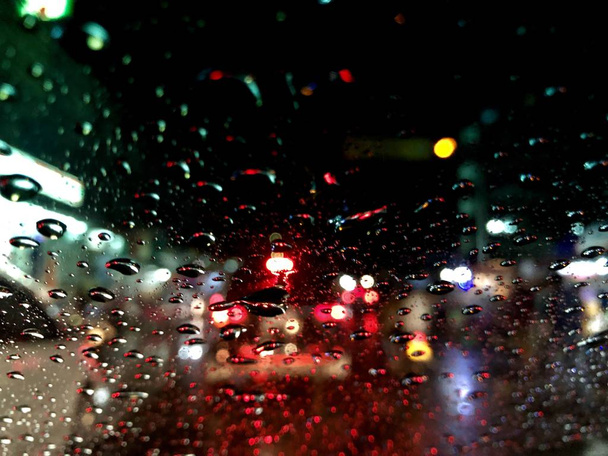 Розфокусоване зображення, барвисте боке з вуличним світлом вночі, падіння на вітровому склі автомобіля. Водіння автомобіля в сильному дощовому штормі. Рух по місту в дощовий день
. - Фото, зображення